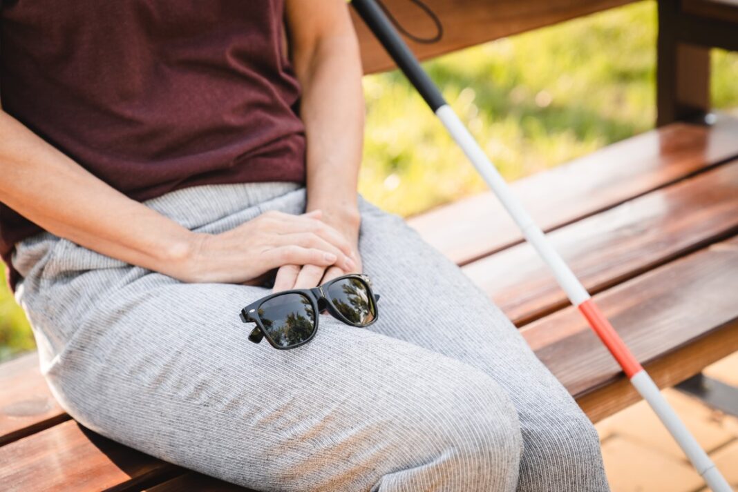 Blind Person Sitting Outdoors with Sunglasses and White Cane on Bench
